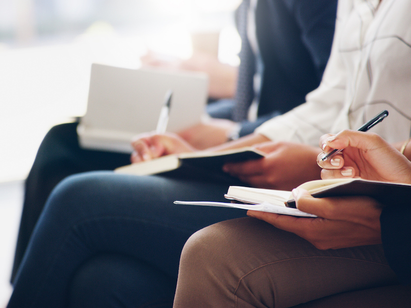 Cropped shot of unrecognizable businesspeople sitting and writing notes in a book while in the office during the day