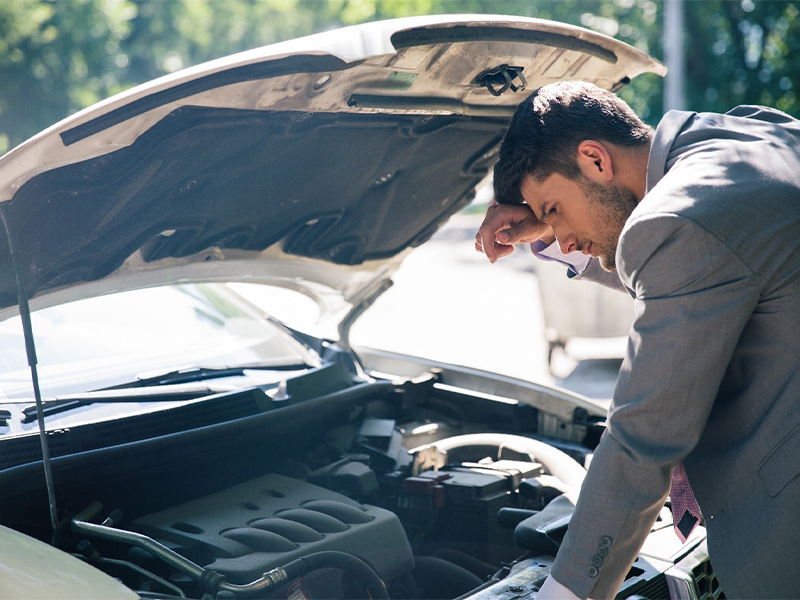 Young man looking under the hood of breakdown car