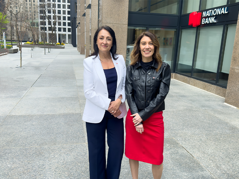 2 professional women from National Bank standing outside next to each other outside the National Bank office.